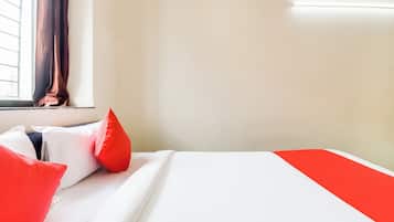 A hotel room with a bed, pillows, a window with curtains, and a wall-mounted light.