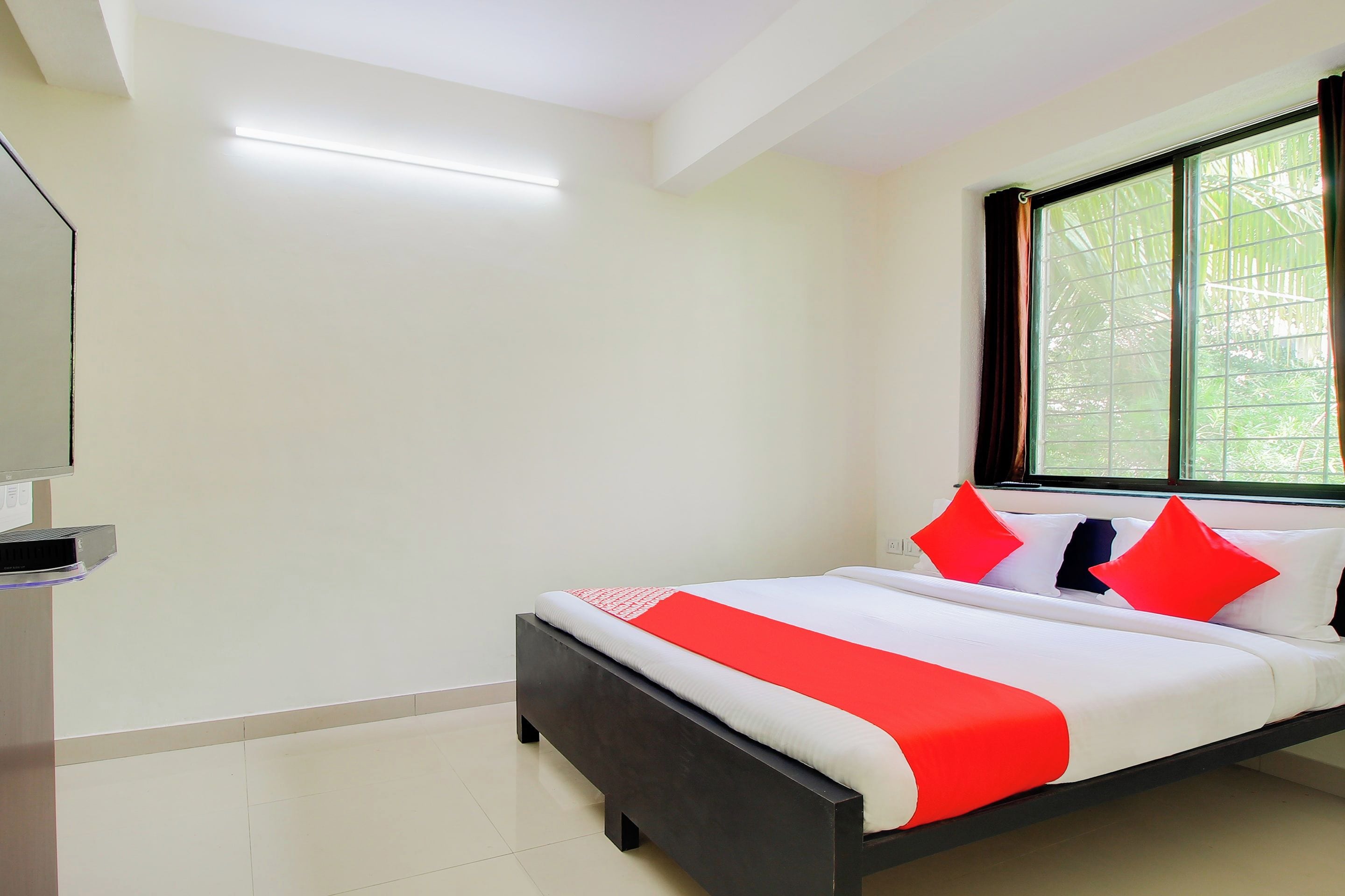 Une chambre à coucher avec un lit, une fenêtre avec des rideaux et un téléviseur à écran plat posé sur un meuble.