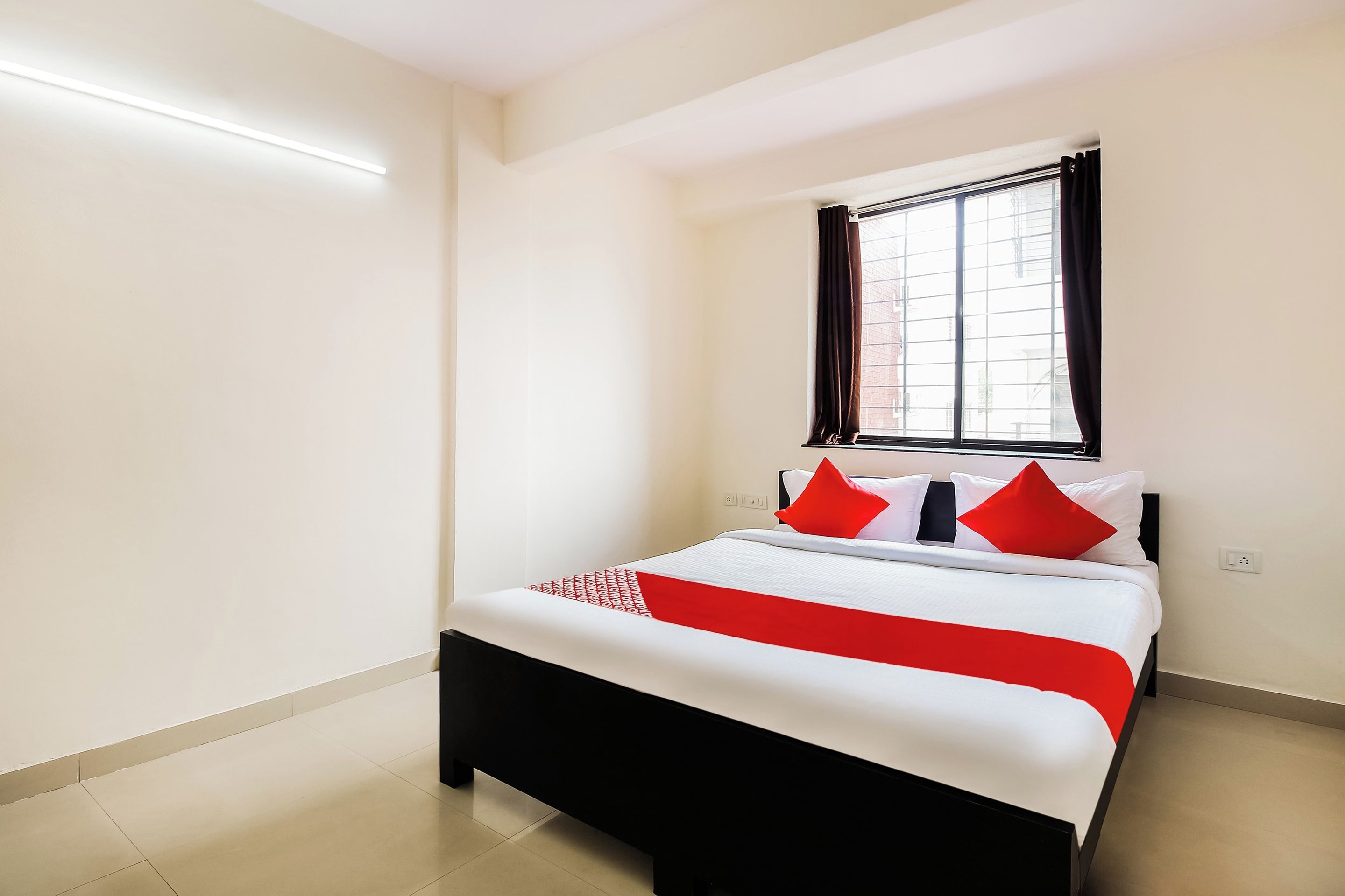A hotel room with a bed, a window with curtains, and a light fixture on the wall.