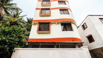 A multi-story building with a white facade and orange accents, featuring multiple windows with metal grilles.
