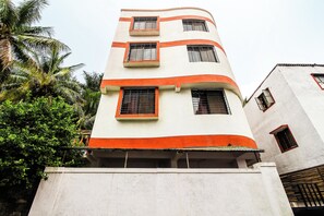 A multi-story building with a white facade and orange accents, featuring multiple windows with metal grilles. - Hotel O Galaxy Near INOX (Pune)