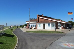 A building with a brick facade, a covered entrance, and a flagpole with flags. - Holiday apartment with 1 bedroom (Büsumer Deichhausen)
