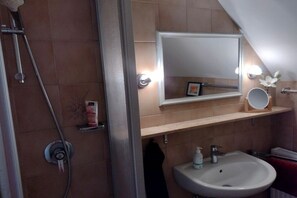 Een badkamer met een douche, een wastafel, een spiegel en een handdoekhouder.