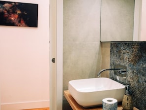 Un baño con un lavamanos blanco, un rollo de papel higiénico y una pared con textura.