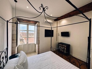 Quarto com cama de dossel, televisão na parede e janela com vista para um telhado de azulejos.
