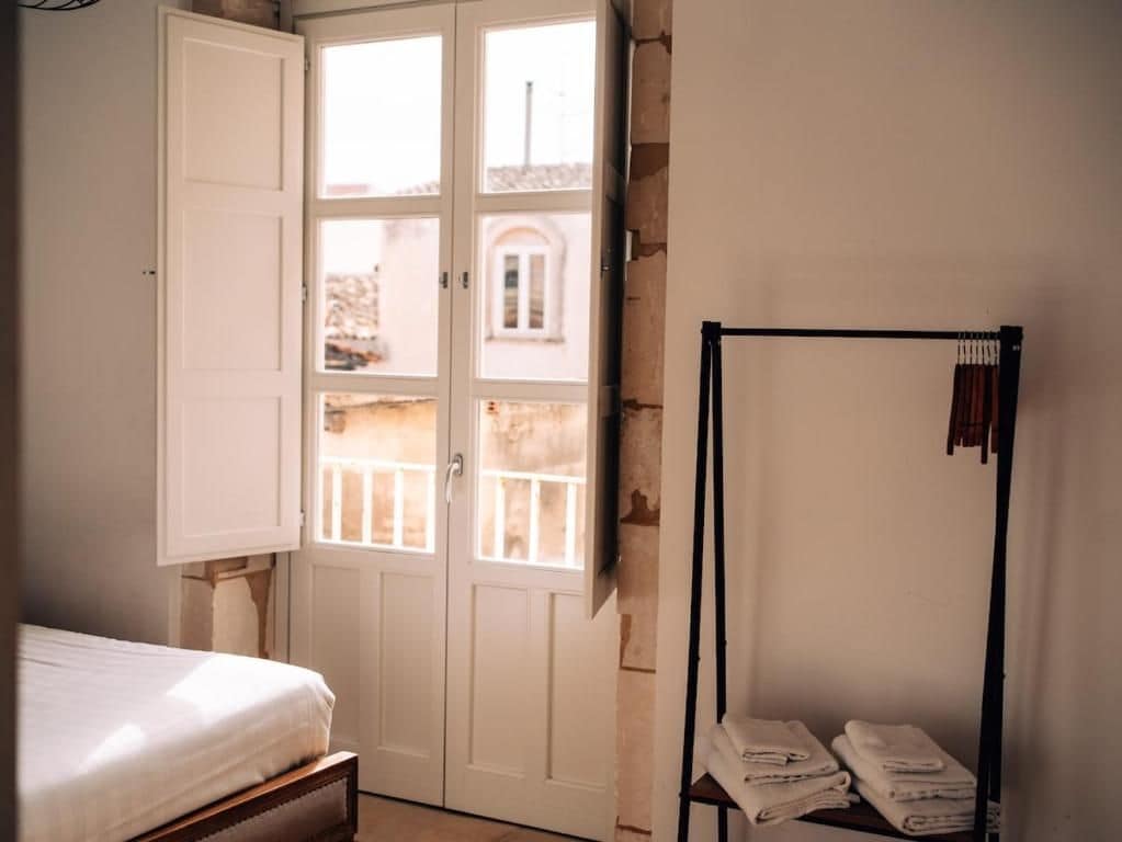 Un dormitorio con cama, armario, puerta que da a un balcón y un perchero con toallas dobladas.