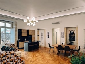 Un espacio habitable moderno con suelo de espiga, una zona de comedor con mesa y sillas de madera, una cocina con estufa integrada y un amplio ventanal que proporciona luz natural.