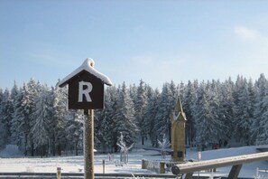 A snow-covered landscape with a sign indicating a parking area, a small building, and a snow-covered forest in the background. - Benni's Toboggan Run (Oberhof)