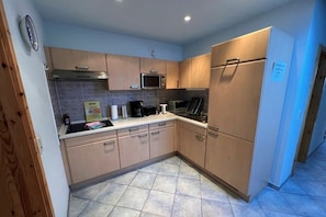 A compact kitchen with wooden cabinets, a microwave, a stove, and a refrigerator. - Benni's Toboggan Run (Oberhof)