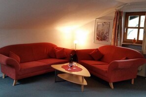 A red sofa set with a small table in between, a lamp on the wall, and a window with curtains. - Adalbert Stifter Holiday Village (Hauzenberg)