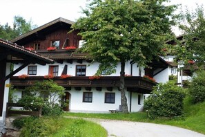 A traditional chalet with a sloped roof, wooden balconies, and a large tree in front. - Adalbert Stifter Holiday Village (Hauzenberg)