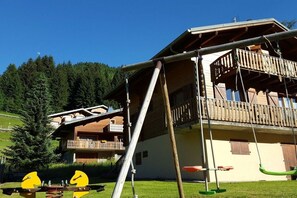 A chalet with a balcony, a wooden deck, and a swing set.