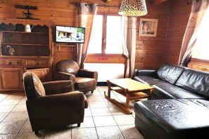 A cozy room with a leather sofa, armchairs, a wooden coffee table, and a television on the wall.