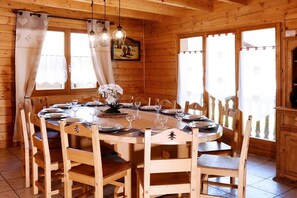 A wooden dining room with a round table set for six, surrounded by wooden chairs.