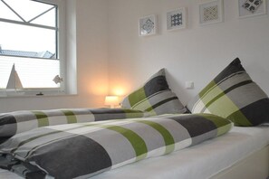 Ein Bett mit gestreifter Bettwäsche und Kissen, ein Fenster mit Jalousien und gerahmte Kunstwerke an der Wand.