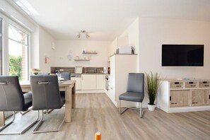 A modern living room with a dining area, a kitchen in the background, and a TV mounted on the wall. - Holiday apartment with 2 bedrooms (Norddeich)