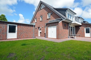 A two-story brick house with a balcony, a garage, and a well-maintained lawn. - Holiday apartment with 2 bedrooms (Norddeich)