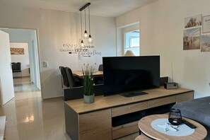 En moderne stue med et fladskærms-tv, møbler i træ, en vægmonteret lampe og et dekorativt kunstværk.