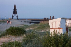 A beach with a large wooden structure, a wicker chair, and a small building. - Holiday apartment with 2 bedrooms (Cuxhaven-Duhnen)