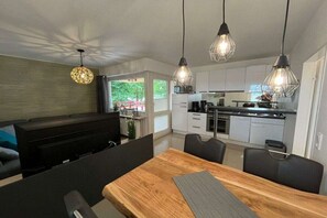 Een moderne keuken met witte kastjes, een eethoek met een houten tafel en hanglampen.