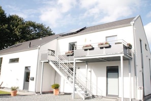 A two-story building with a white exterior, a staircase leading to the upper floor, and a number '28' on the right side. - Holiday apartment in Husum with swimming pool (Husum)