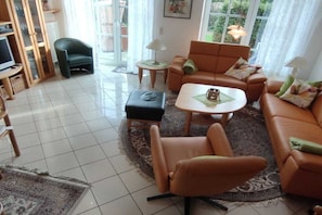 A living room with a sofa, armchair, ottoman, coffee table, and a television. - Holiday home with 4 bedrooms (Carolinensiel)