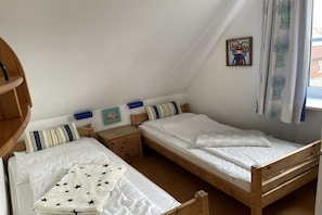 A bedroom with two single beds, wooden headboards, a nightstand, a small table, and a wall-mounted picture. - Holiday home with 4 bedrooms (Carolinensiel)