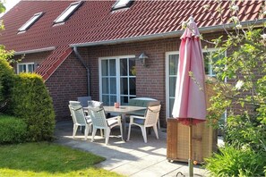 Une terrasse avec une table et des chaises, un fauteuil en osier et un parasol rose.