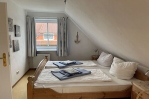 Une chambre avec deux lits, une fenêtre avec des rideaux, un radiateur et un luminaire fixé au mur.