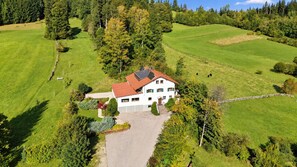 A white building with a red roof, surrounded by green fields and trees, with a paved driveway leading to the entrance. - Modern Apartment with Stunning Mountain Views @ Sunrise Pfronten (Pfronten)