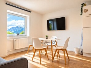 Una cocina moderna con zona de comedor, un amplio ventanal con vista a la montaña y un televisor de pantalla plana montado en la pared.
