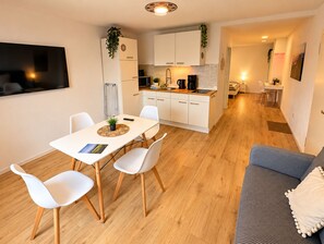 Et moderne køkken med hvide skabe, et spiseområde med bord og stole, og en stue med en sofa.