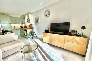 Ett modernt vardagsrum med en soffa, en tv placerad på ett träskåp och en matplats med ett kök synligt i bakgrunden.