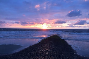 A beach scene with a pebbly shore leading to the sea, under a sunset sky. - Beach Villa Atlantic Apt. 2 (Norderney)