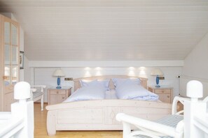 A bedroom with a wooden bed, two bedside tables with lamps, and a white chair. - Beach Villa Atlantic Apt. 2 (Norderney)