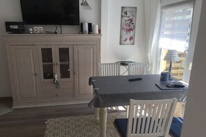 Ein Essbereich mit Tisch, Stühlen, einem Fernseher über dem Schrank und einem Fenster mit Jalousien.