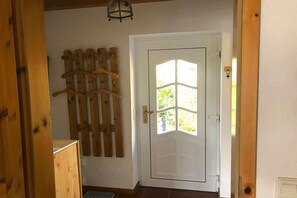 A room with a wooden door, a coat rack with hangers, and a light fixture above the door. - Holiday home with 2 bedrooms (Wangerland \/ Hooksiel)