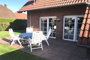 Een terras met een tafel en stoelen, een bakstenen muur en een schuifpui.