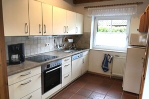 Een keuken met witte kasten, een inbouwoven, een vaatwasser en een raam met uitzicht op groen.