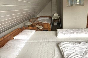 A room with two beds, a wicker chair, a small table with a lamp, and a window. - Holiday home with 2 bedrooms (Wangerland \/ Hooksiel)
