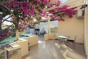 An outdoor patio area with a table and chairs, a pergola with flowering vines, and a view of a pool. - Villa in Pitsidia with swimming pool (Pitsidia)