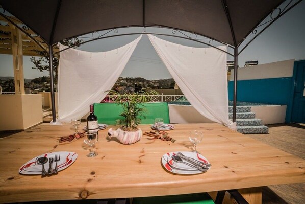 A dining table set for two with a tent overhead, a potted plant, and a bottle of wine. - Villa in Pitsidia with swimming pool (Pitsidia)