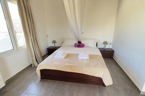 A bedroom with a large bed, two bedside tables, a window with curtains, and a view of the outside. - Villa in Pitsidia with swimming pool (Pitsidia)