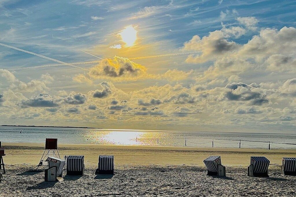 Una playa con sillones de descanso y una estela de avión en el cielo.