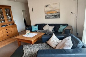 Ein Wohnzimmer mit einem dunkelblauen Sofa, einem Holztisch und einer Vitrine.