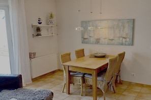 Ein Essbereich mit Holztisch und Korbstühlen, einem Bild an der Wand und einem Regal mit Dekoration.