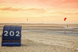 A beach with a blue numbered board, a person in the water, and kites in the sky. - Holiday HOME "North Sea" (Hooksiel)