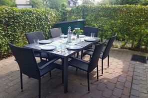 An outdoor patio with a rectangular table set for four, surrounded by wicker chairs. - Holiday apartment Ankerplatz (Cuxhaven)