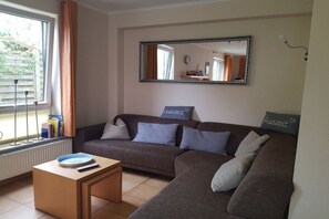 A living room with a brown sofa, a coffee table, a mirror, and a window with curtains. - Holiday apartment Ankerplatz (Cuxhaven)