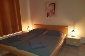 A single bed with a wooden headboard, two bedside tables with lamps, and a painting on the wall. - Holiday apartment Ankerplatz (Cuxhaven)